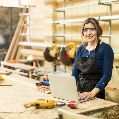 A photo of a female woodworker with her laptop in a workshop